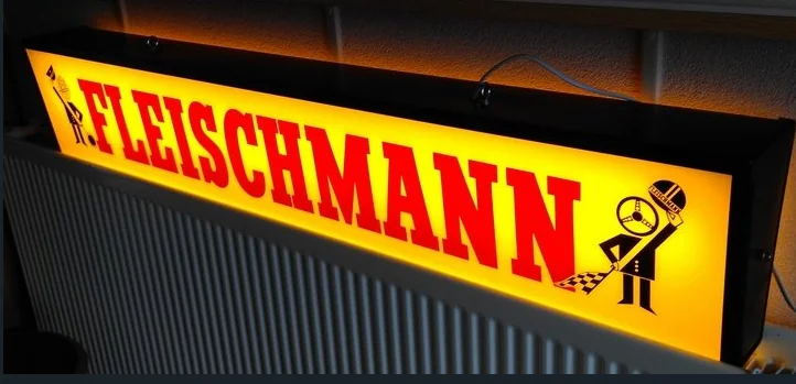 Gelbe Fleischmann-Leuchtreklame mit rotem Schriftzug und Flaggenmännchen, eingeschaltet