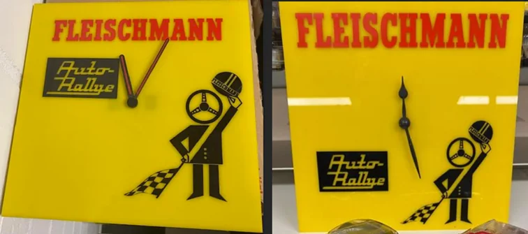 Zwei gelbe Fleischmann-Wanduhren im Vergleich, links mit roten Zeigern, rechts mit schwarzen Zeigern